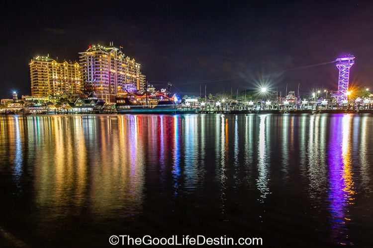 A night image of Destin Harbor showing Emerald Grande and the Harborwalk zip line towers