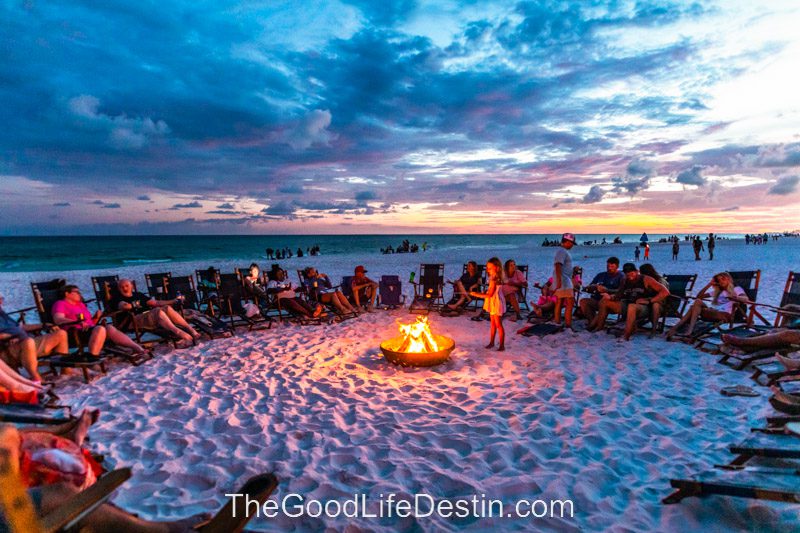 People gathered around the beach bonfire at Royal Palm Grill at sunset in Miramar Beach