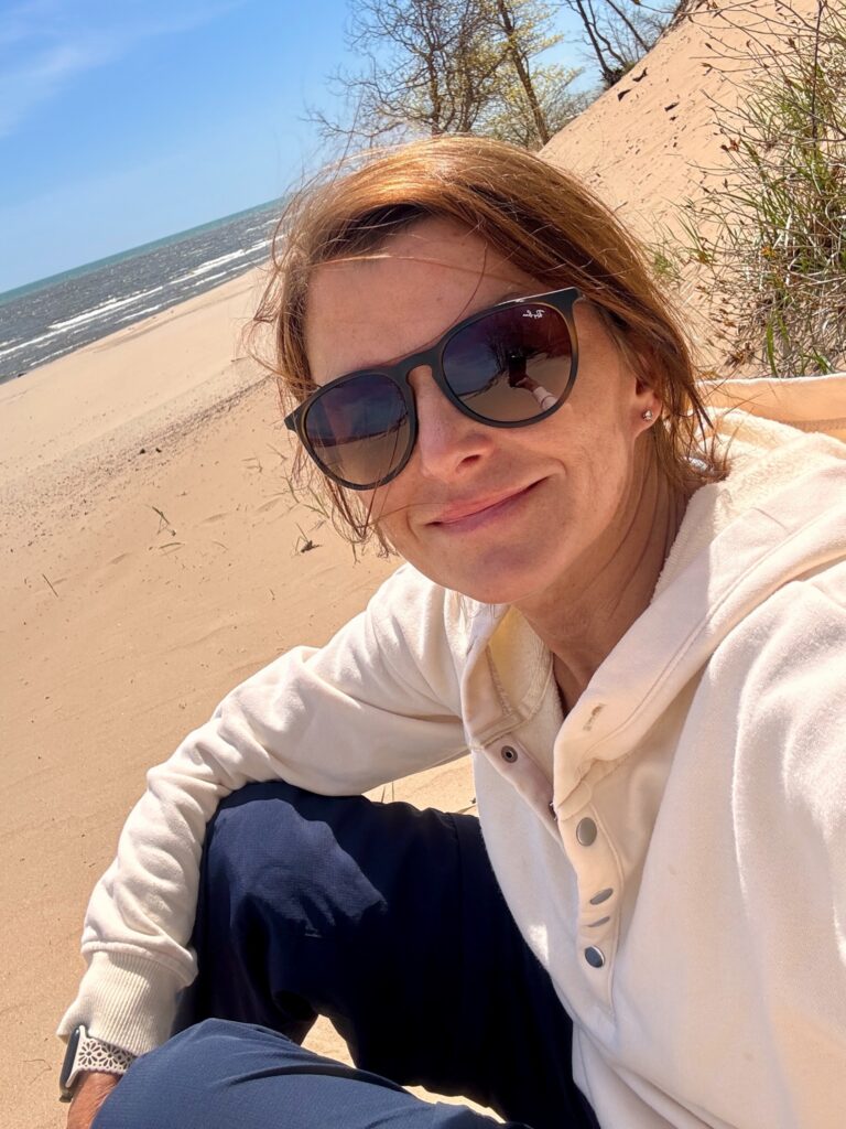 Woman in sunglasses and a white hoodie taking a selfie on a sandy beach